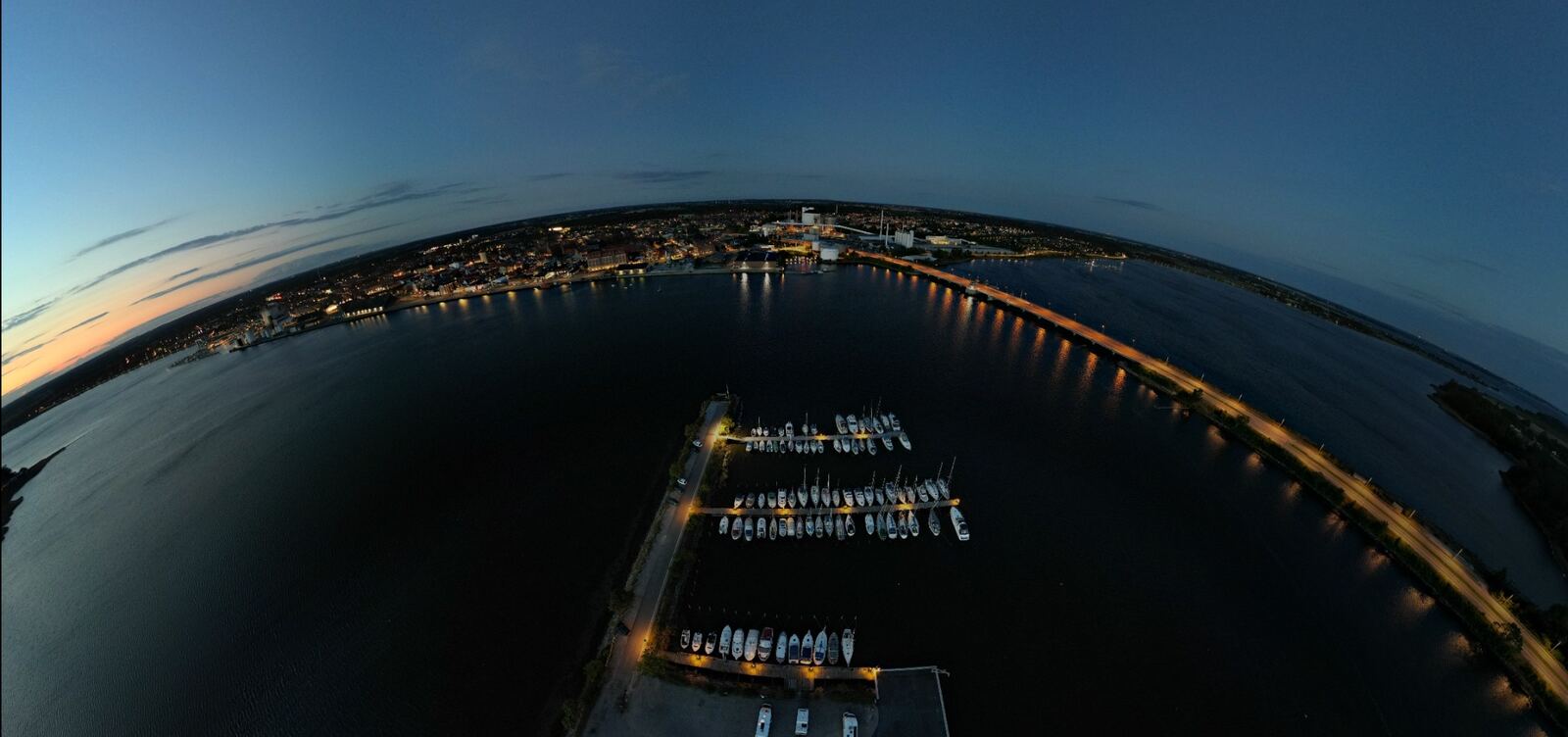 Oplyst bro og havn set som panorama om aftenen